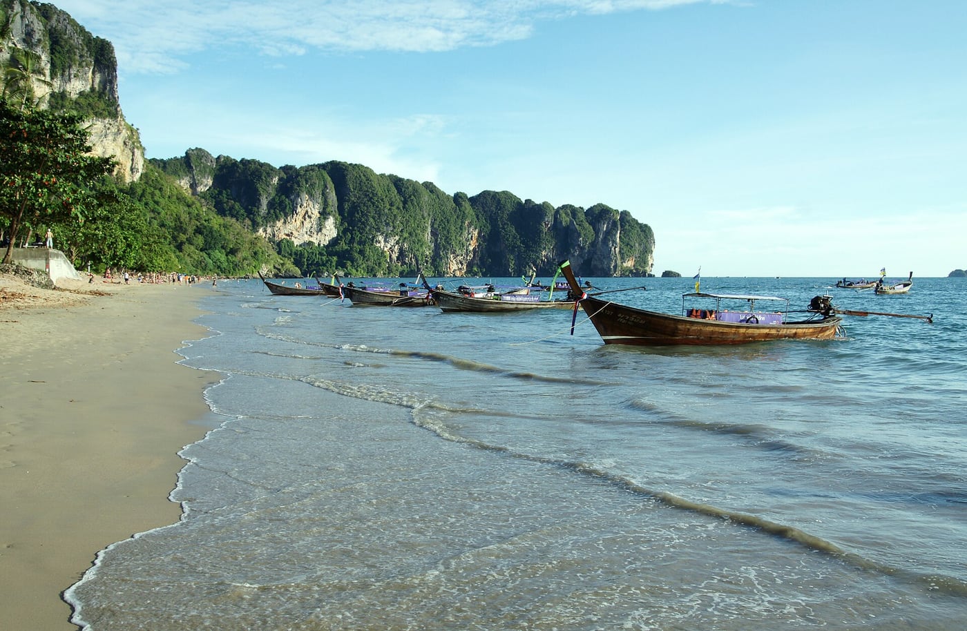 Long-tail boats moored in the shallows at Ao Nang Beach, with coastal cliffs behind