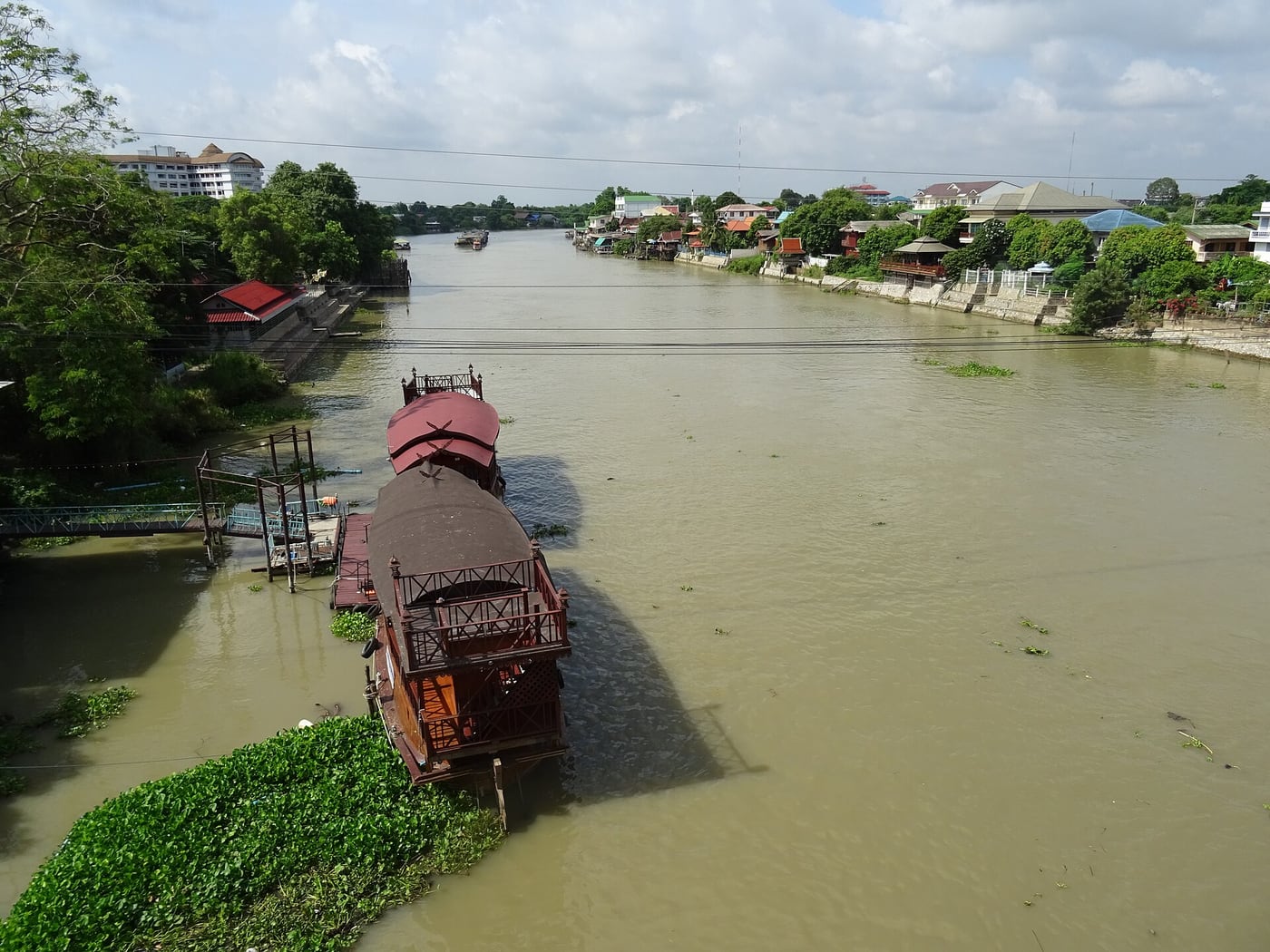 A roofed boat moored on the Pa Sak River in Ayutthaya, with buildings along both banks