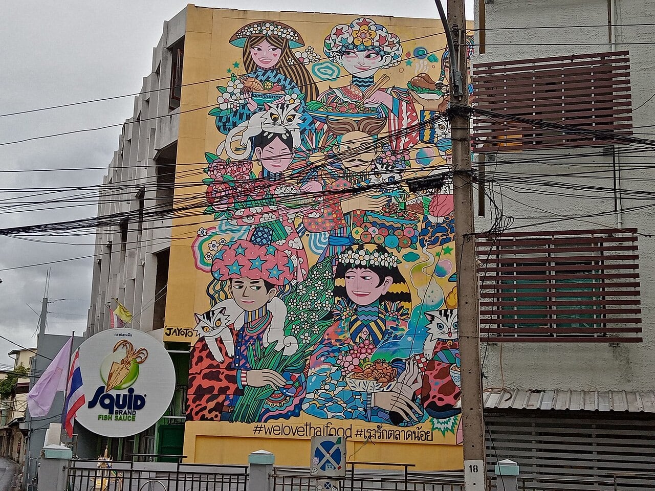 A mural of figures and cats on a fish sauce factory wall in Talat Noi