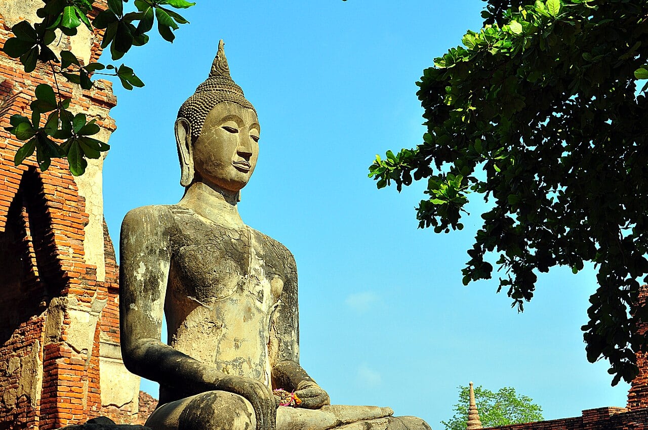 A seated stone Buddha beside brick ruins at Wat Mahathat in Ayutthaya