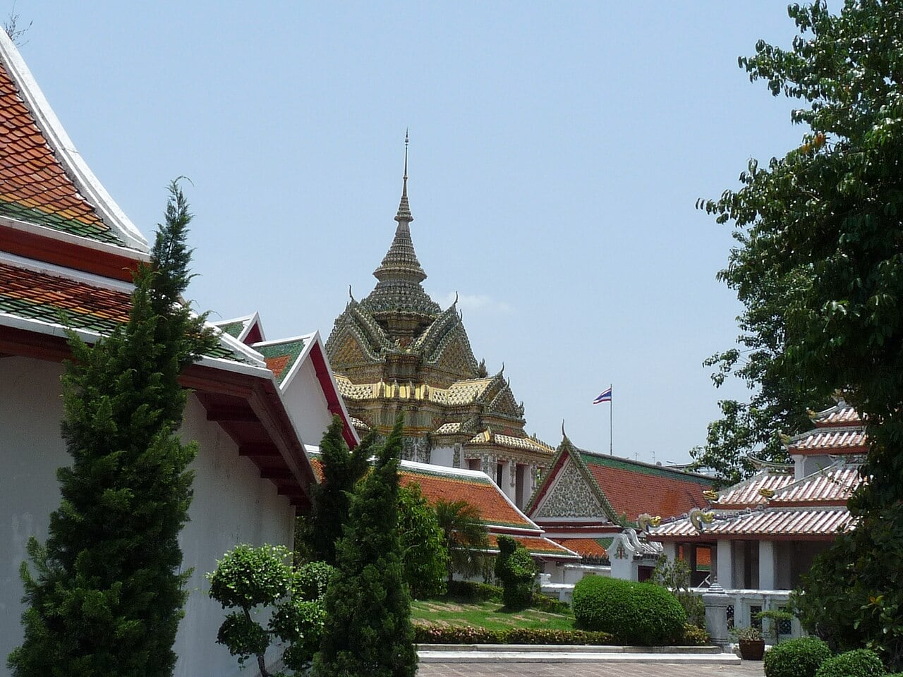 Temple roofs, an ornate spire and trees in a courtyard at Wat Pho