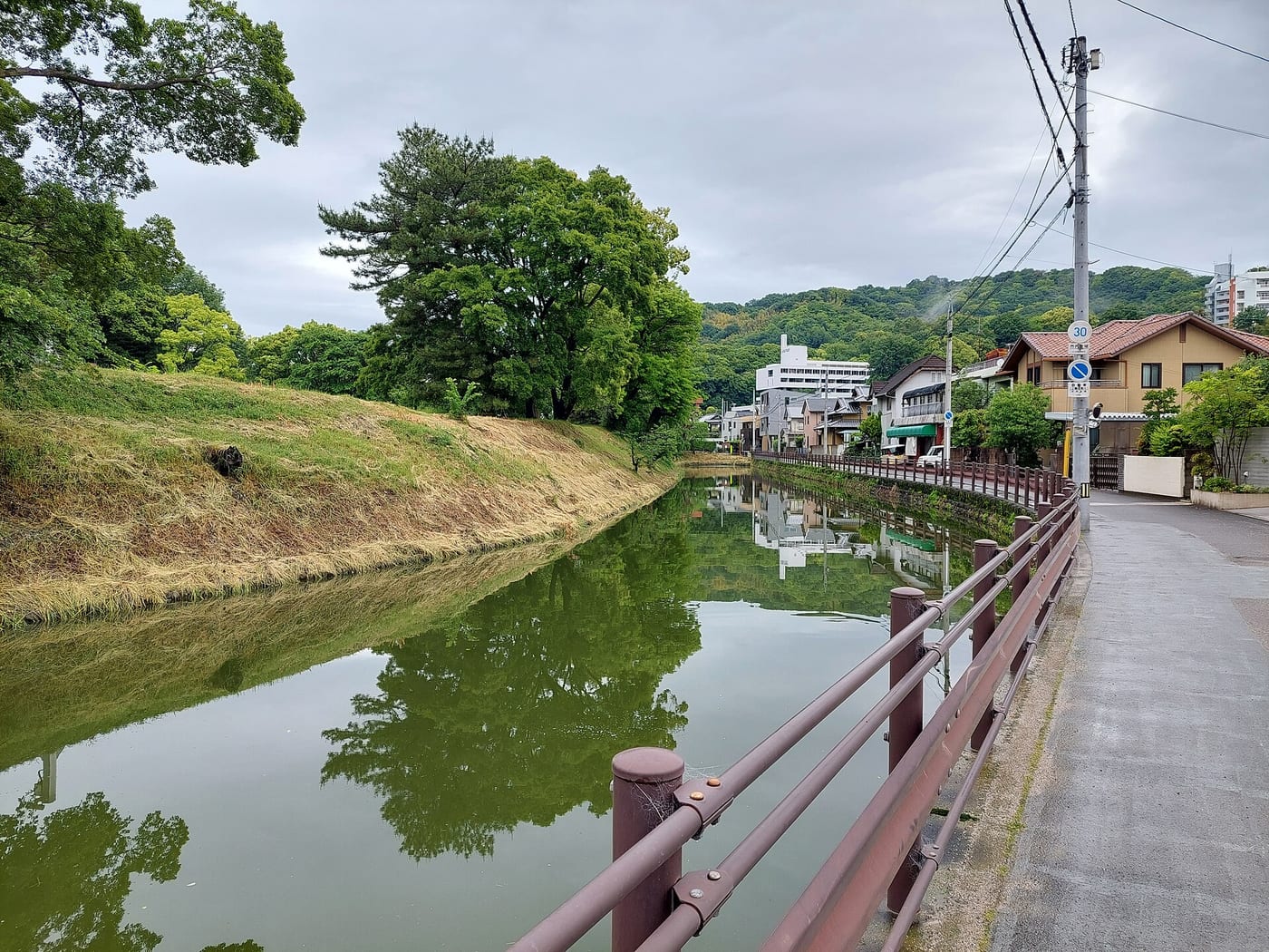 The moat and waterside path beside the greenery of Yuzuki Castle ruins in Dogo Park